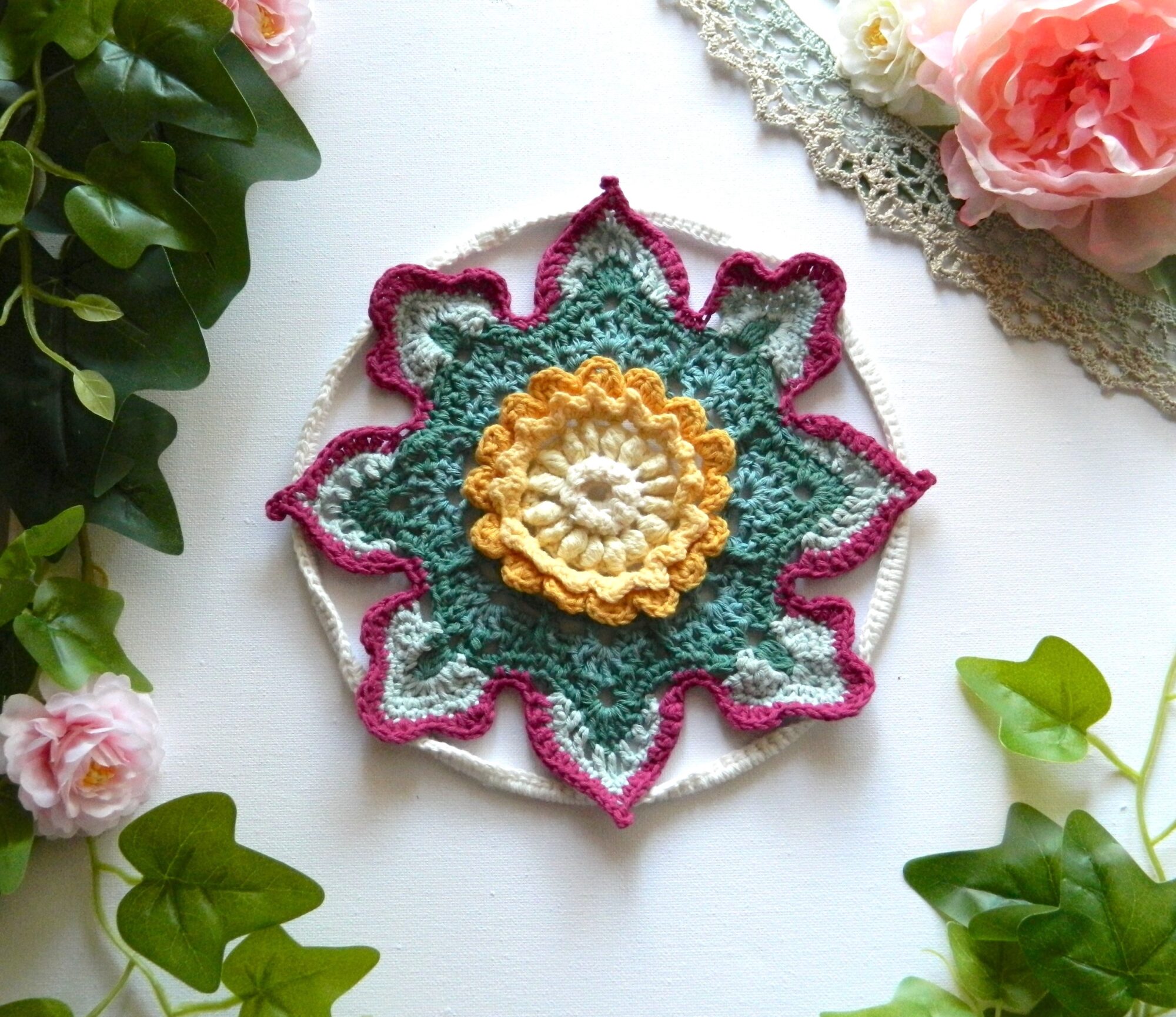 Attrape-rêves fleur au crochet BLOM Attrape-rêves au crochet en forme de fleur dans des tons vert, crème, jaune et fuchsia.