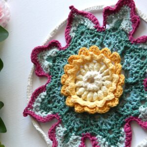 Attrape-rêves fleur au crochet BLOM - vue artistique gauche Attrape-rêves au crochet en forme de fleur dans des tons vert, crème, jaune et fuchsia.