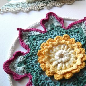 Attrape-rêves fleur au crochet BLOM - vue artistique droit Attrape-rêves au crochet en forme de fleur dans des tons vert, crème, jaune et fuchsia.