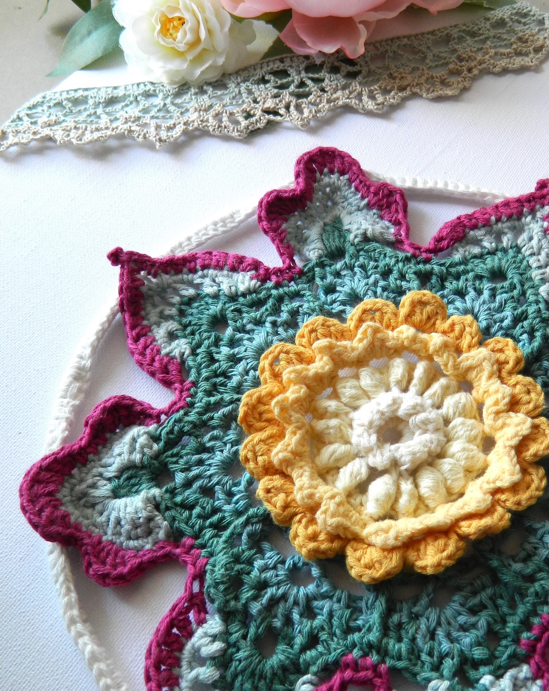 Attrape-rêves fleur au crochet BLOM - vue artistique droit Attrape-rêves au crochet en forme de fleur dans des tons vert, crème, jaune et fuchsia.