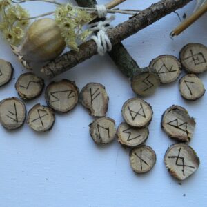 Gros plan sur un jeu de 24 runes en chêne gravées à la main selon le Futhark ancien, présenté dans une composition naturelle.