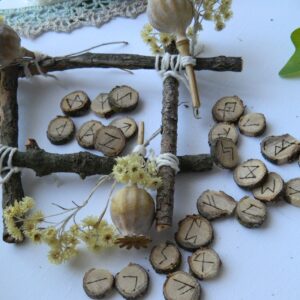 Jeu de runes en chêne gravées à la main, disposé dans une mise en scène naturelle avec branches, fleurs séchées et éléments végétaux.