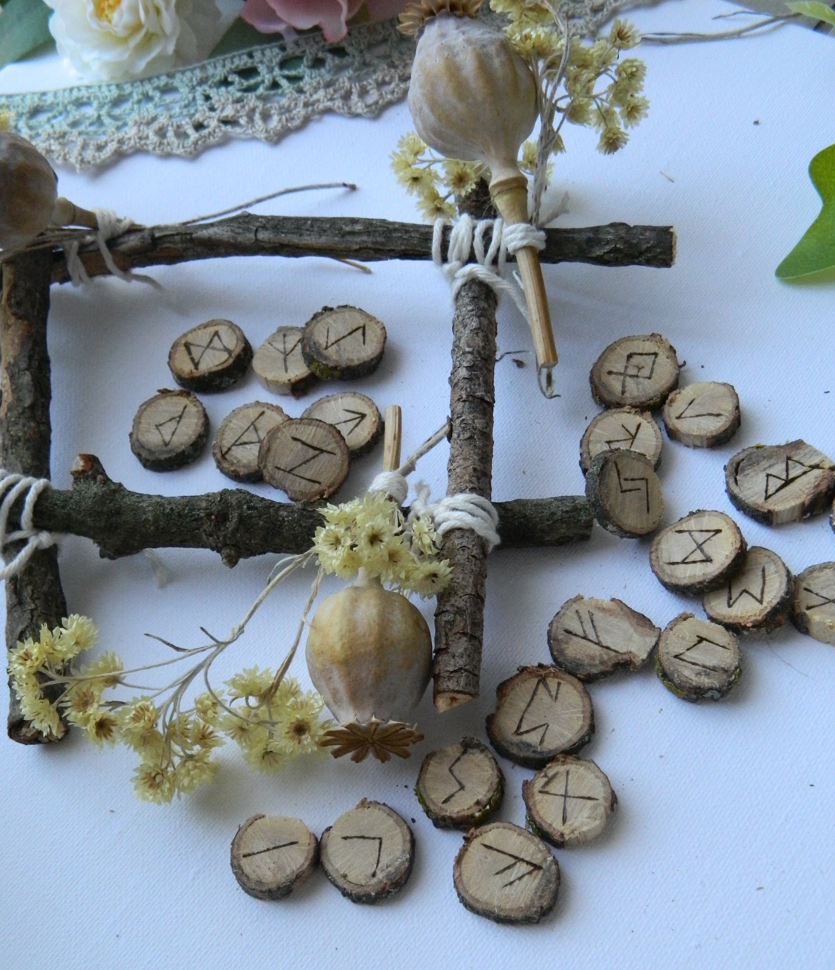 Jeu de runes en chêne gravées à la main, disposé dans une mise en scène naturelle avec branches, fleurs séchées et éléments végétaux.
