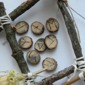 Runes en chêne – artisanat spirituel Runes en chêne gravées à la main disposées dans une composition naturelle évoquant les traditions nordiques et la pratique divinatoire.